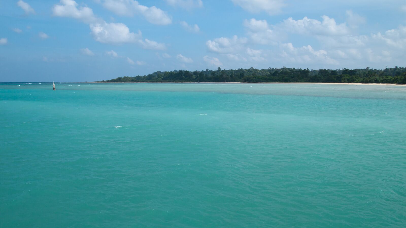 Clear turquoise water in a bay off Neil Island, with a low forested shore on the horizon